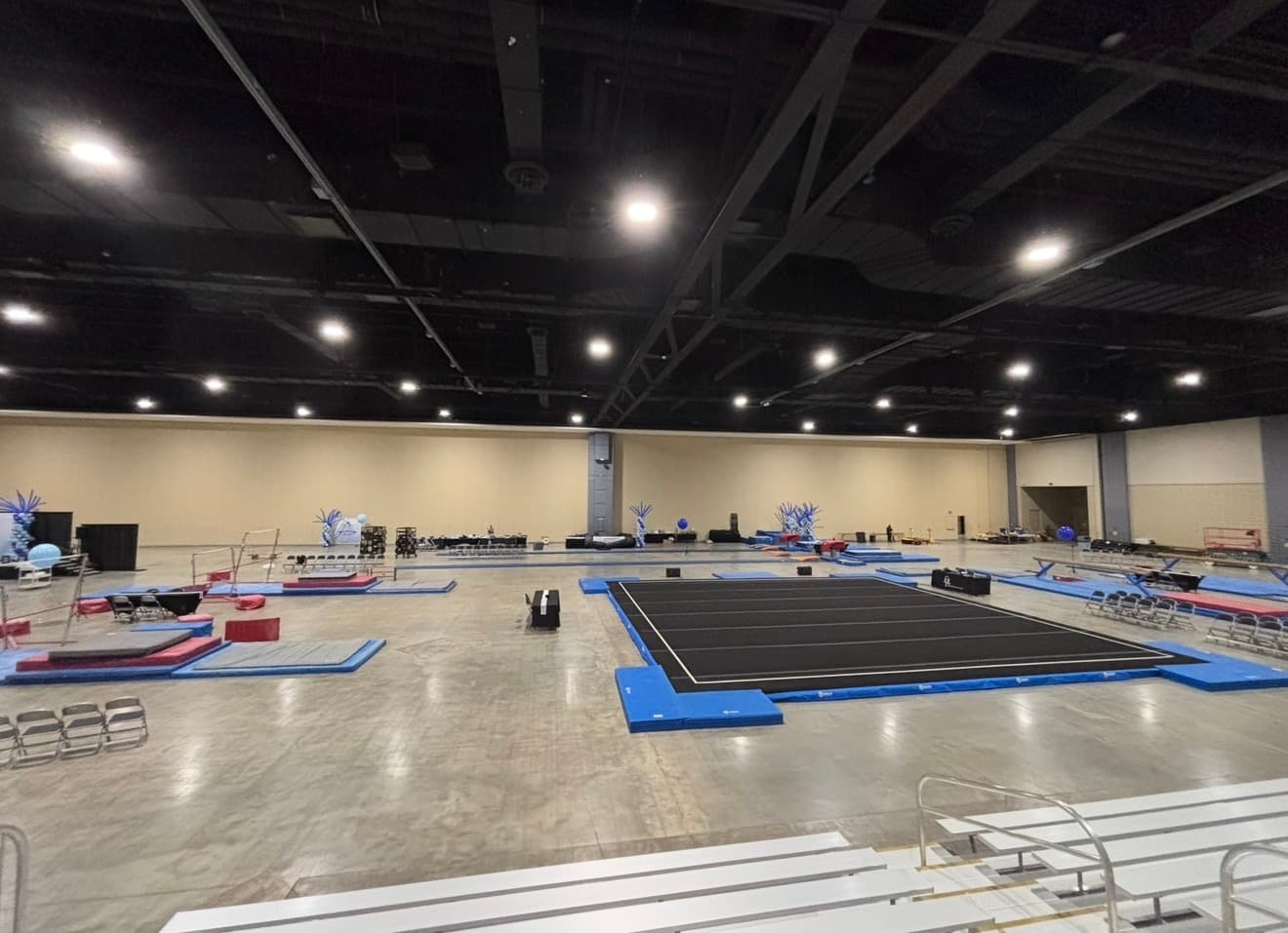 Wide view of a competition floor, bars, and beam laid out across a convention center hall.